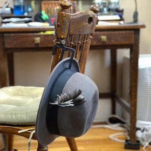 May include: A gray fedora hat with a black band and a feather accent hanging on a wooden chair.
