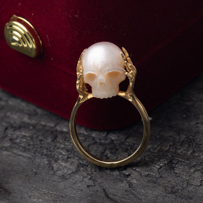 May include: A gold ring with a pearl skull design. The skull is white and the ring is a shiny gold.