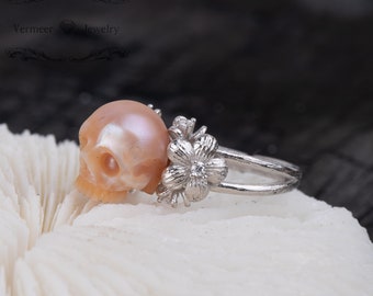 Puede incluir: Un anillo de plata con una calavera de perla rosa y una flor de plata con un pequeño diamante en el centro.