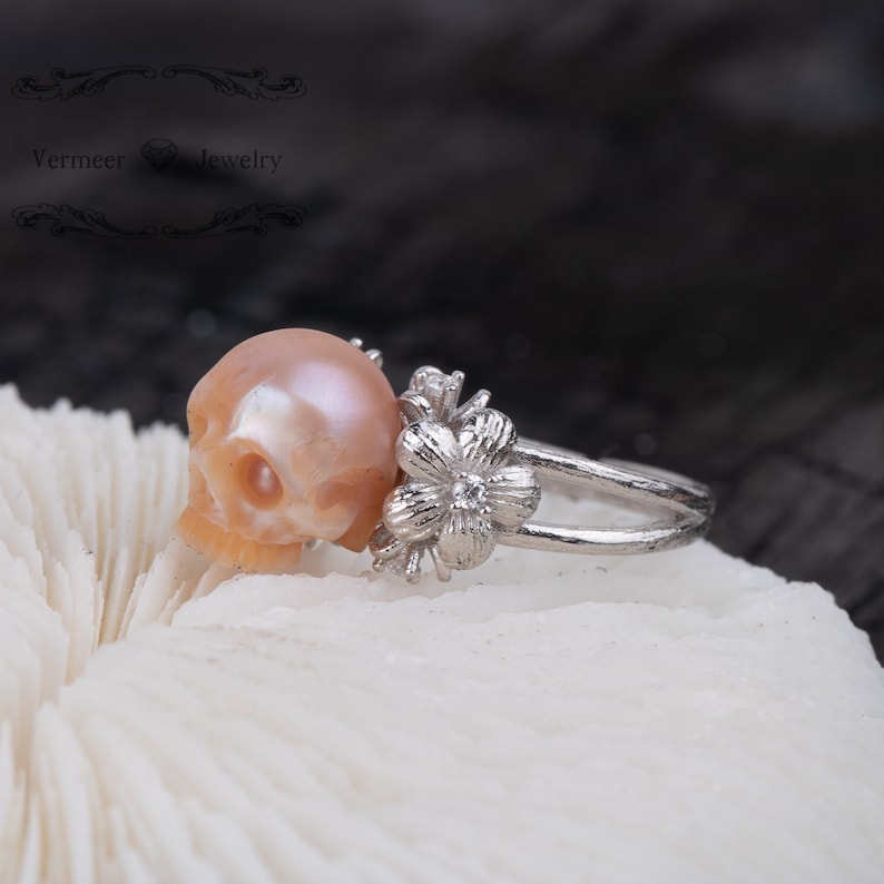 May include: A silver ring with a pink pearl skull and a silver flower with a small diamond in the center.
