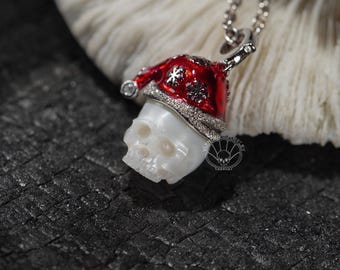 Puede incluir: Colgante de collar de plata con una calavera que lleva un gorro de Papá Noel rojo con detalles de copos de nieve. La calavera es blanca y el gorro está adornado con una banda con forma de diamante. El colgante está en una cadena de plata.