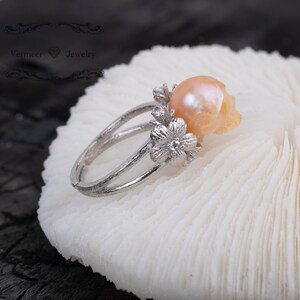 May include: A silver ring with a delicate floral design and a large, pearlescent pink skull-shaped pearl.
