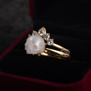 Op de afbeelding: Een gouden ring met een witte schedel en een kroon van heldere zirkonia stenen.