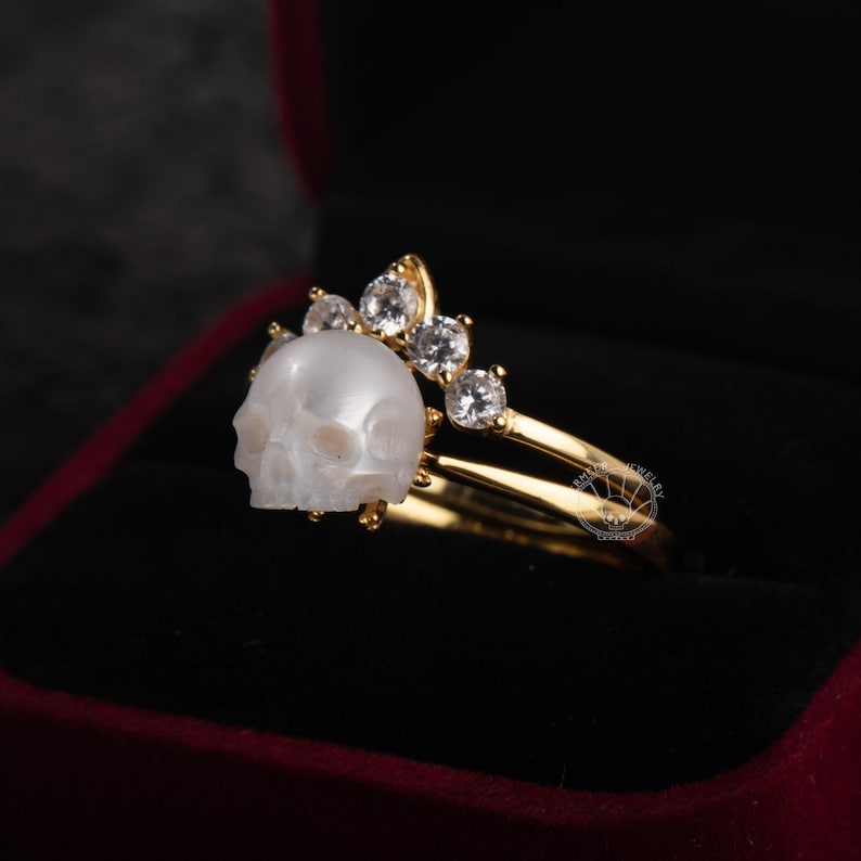 Op de afbeelding: Een gouden ring met een witte schedel en een kroon van heldere zirkonia stenen.