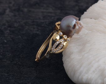 May include: A gold ring featuring a pearl skull design. The ring is set with small clear stones and is displayed on a white background.