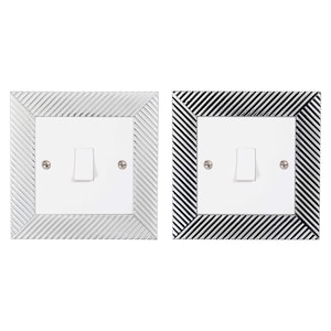 May include: Two light switch covers with a decorative, diagonal striped pattern. One cover is silver and the other is black.