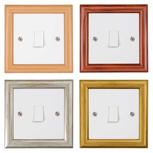 May include: Four light switch covers in different wood frames. The frames are natural wood, red wood, silver, and gold.