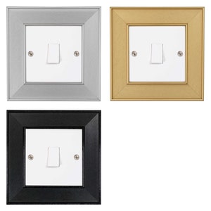 May include: Three light switch covers in different colours: silver, gold, and black. Each cover has a white light switch with a toggle.