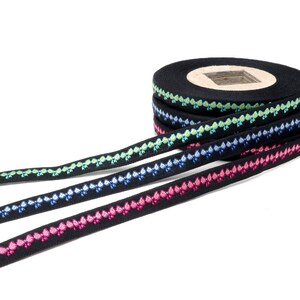Peut inclure: Un rouleau de ruban noir avec une bordure décorative de fleurs brodées colorées. Le ruban est disponible en quatre couleurs : rose, bleu, vert et jaune.