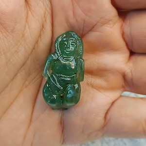 Puede incluir: Una pequeña talla de jade verde de una mujer con un rostro detallado y ropa intrincada. La talla es lisa y pulida.