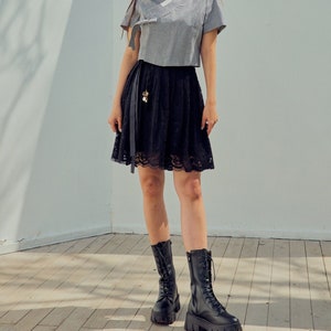 May include: A woman wearing a gray and white striped top with a black lace skirt and black lace-up boots. The top has a traditional Korean style with a collar and a tie at the front.
