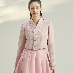 May include: A light pink two-piece outfit. The jacket is a cropped style with a V-neck and decorative buttons. The skirt is a midi length with a pleated design. The outfit is made of a textured fabric.