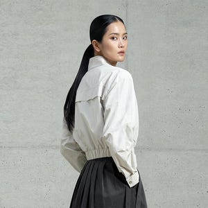 May include: A woman wearing a white, long-sleeved shirt with a gathered waist and a black skirt.