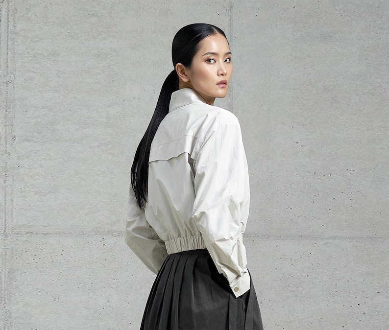 May include: A woman wearing a white, long-sleeved shirt with a gathered waist and a black skirt.
