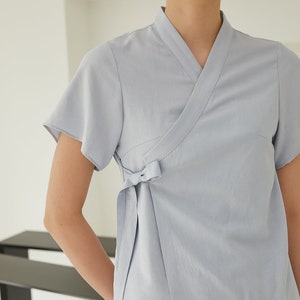 May include: A light blue wrap top with short sleeves and a tie at the waist.
