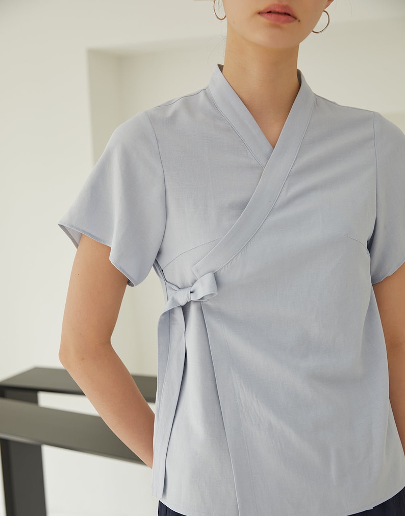 May include: A light blue wrap top with short sleeves and a tie at the waist.