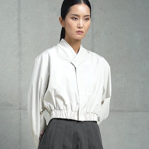May include: A white cropped blouse with a long sleeve and a gathered elastic waistband. The model is wearing a black pleated skirt and is 5'9" tall.