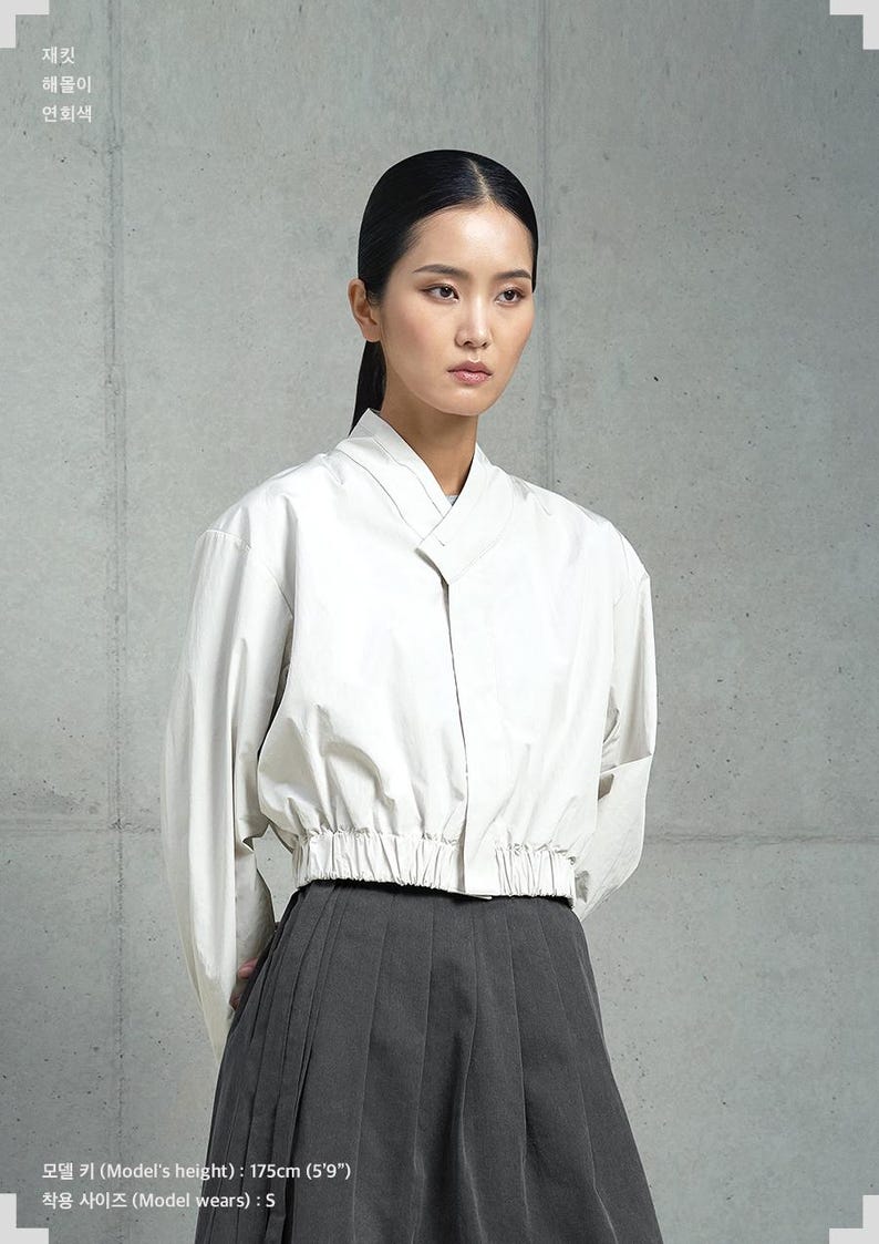 May include: A white cropped blouse with a long sleeve and a gathered elastic waistband. The model is wearing a black pleated skirt and is 5'9" tall.