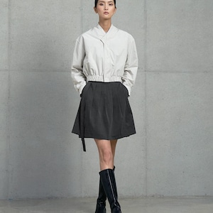 May include: A woman wearing a white collared shirt with a black skirt and black knee-high boots. The shirt has a cinched waist and the skirt has a pleated design.
