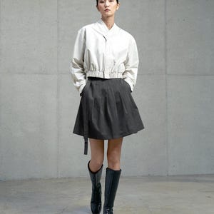 May include: A woman wearing a white, cropped, button-up shirt with a black skirt and black knee-high boots.