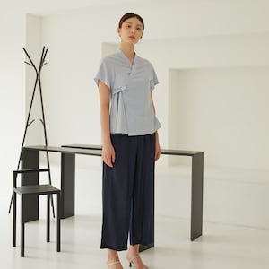 May include: A light blue blouse with a wrap-style front and short sleeves. The blouse is worn with dark blue wide-leg pants and beige heeled sandals.