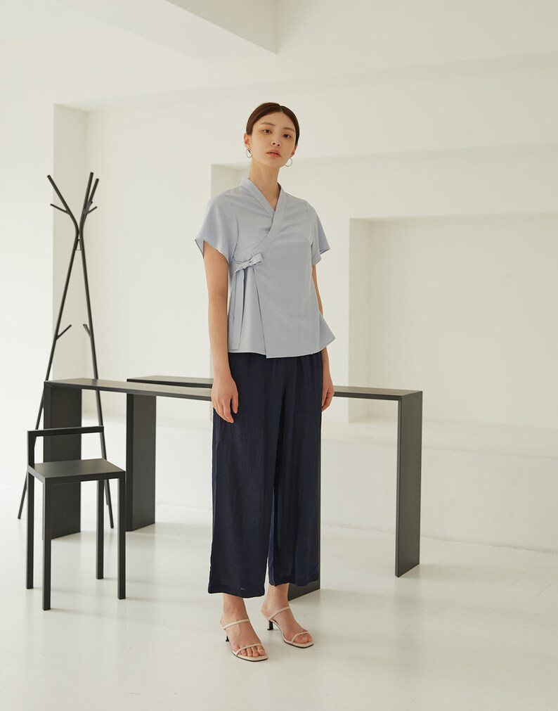 May include: A light blue blouse with a wrap-style front and short sleeves. The blouse is worn with dark blue wide-leg pants and beige heeled sandals.