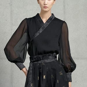 May include: Black ensemble featuring a wrap-style top with sheer sleeves and a matching skirt. The top has a floral patterned trim and the skirt is adorned with gold-colored embellishments. The outfit is cinched at the waist with a coordinating belt.