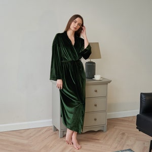 K&ouml;nnte beinhalten: Eine lange, dunkelgr&uuml;ne Samt-Robe mit Schalkragen und einem Bindeg&uuml;rtel. Die Robe wird von einer Person getragen, die in einem Raum mit Holzboden und wei&szlig;er Wand steht.