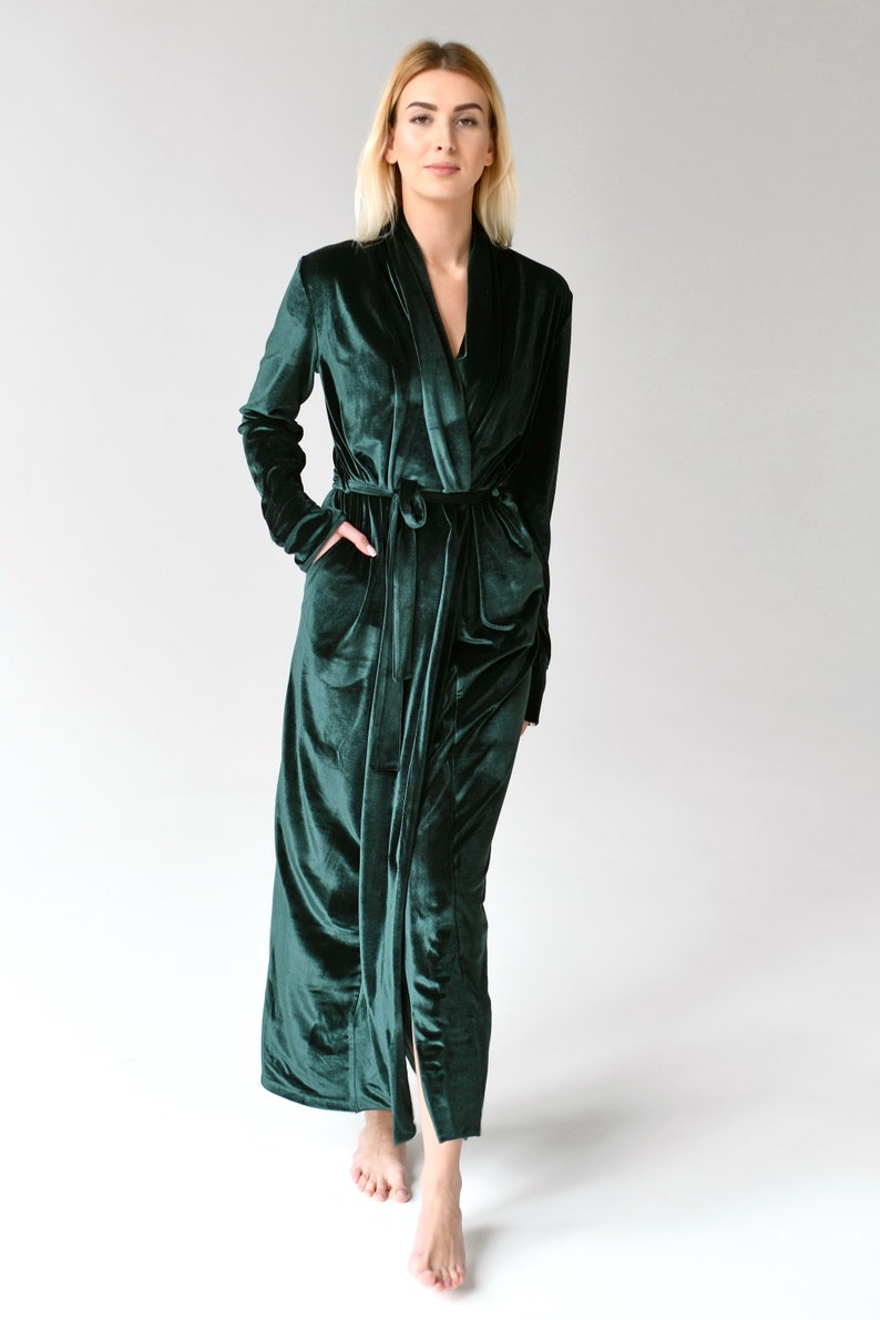 May include: A long, dark green velvet robe with a shawl collar and a tie belt. The robe has long sleeves and pockets.
