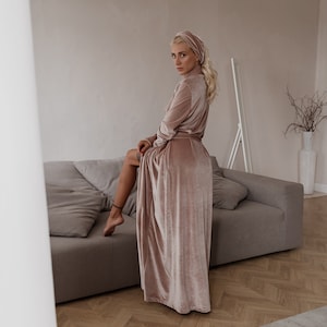 May include: A blush-colored velvet robe and matching head wrap. The long-sleeved robe is belted at the waist and drapes to the floor. The soft, luxurious fabric has a subtle sheen. The robe is worn with a matching head wrap.
