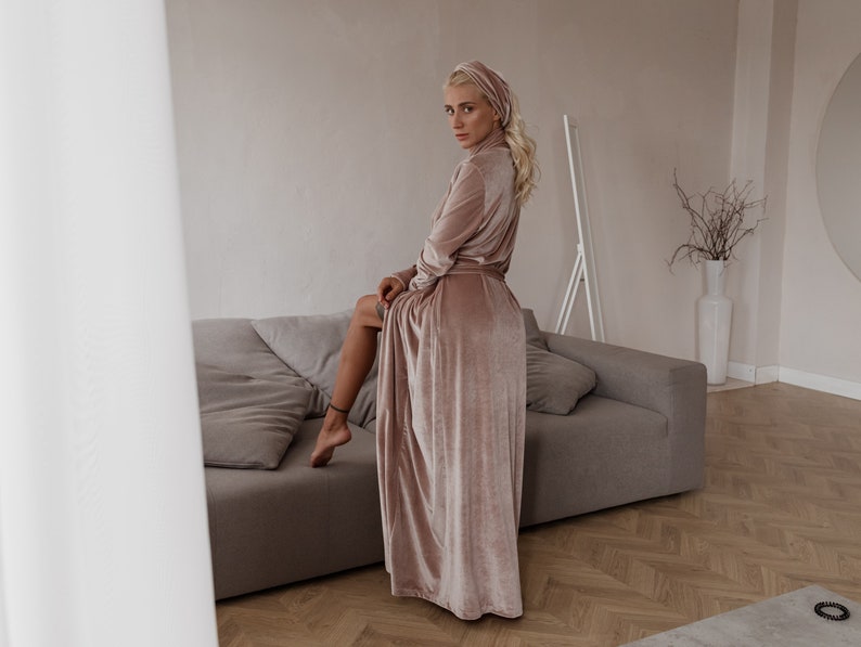 May include: A blush-colored velvet robe and matching head wrap. The long-sleeved robe is belted at the waist and drapes to the floor. The soft, luxurious fabric has a subtle sheen. The robe is worn with a matching head wrap.