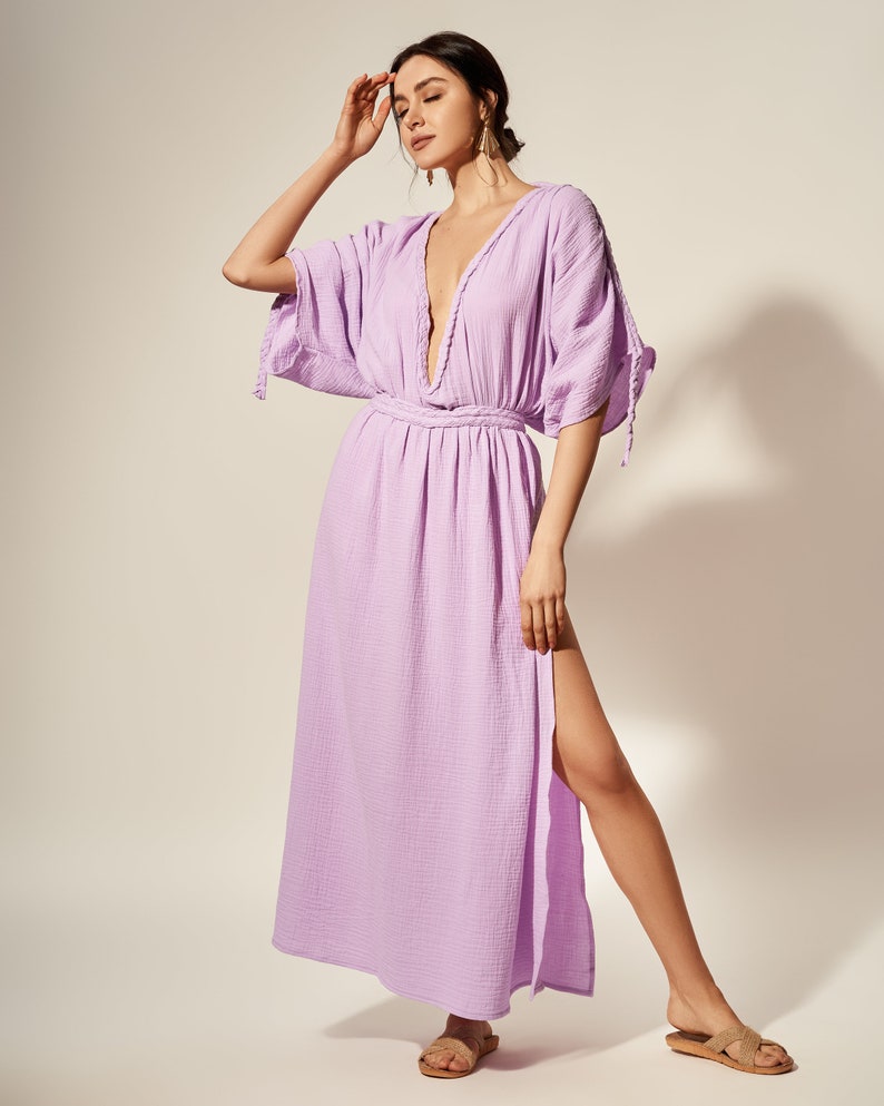 K&ouml;nnte beinhalten: Ein helllilafarbenes Maxikleid mit tiefem V-Ausschnitt, 3/4-&Auml;rmeln und einem Schlitz an der Seite. Das Kleid hat einen Bindeg&uuml;rtel in der Taille und eine lockere Passform.