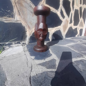 Puede incluir: Una escultura de madera marrón oscuro de un rostro humano con un diseño tallado. La escultura está de pie sobre una superficie plana.