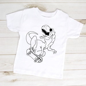 May include: A white t-shirt featuring a black and white illustration of a dinosaur skateboarding. The dinosaur is smiling and has its tongue sticking out.