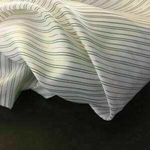 May include: White fabric with thin black and pink stripes. The fabric is folded and draped.