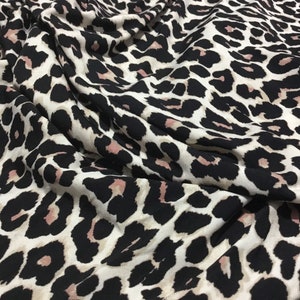 May include: A close-up of a beige fabric with a black and pink leopard print pattern.