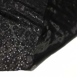 Puede incluir: Tela negra con lentejuelas, doblada para mostrar el lado liso de la tela.
