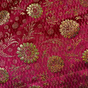 May include: Red velvet fabric with a gold floral pattern. The fabric has a subtle shimmer and a textured surface.