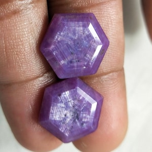 Puede incluir: Dos piedras preciosas hexagonales facetadas de color púrpura con un patrón en forma de estrella.