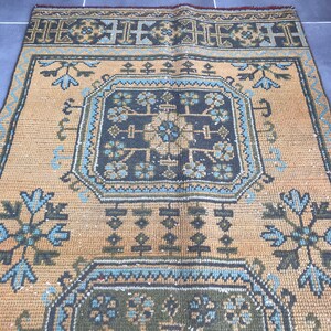 Puede incluir: Una alfombra vintage con un patr&oacute;n geom&eacute;trico en tonos azules, verdes y marrones sobre un fondo beige.