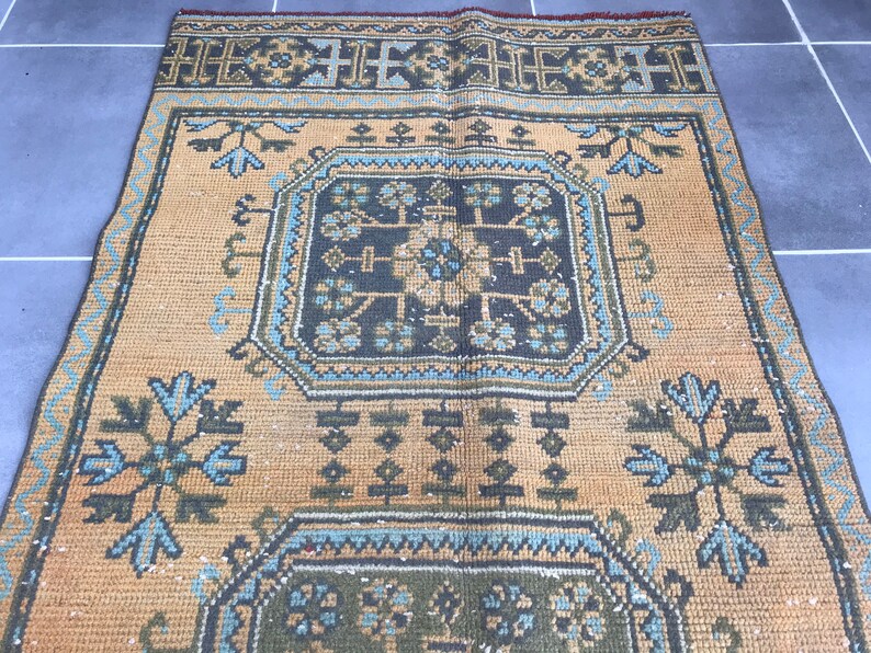 Puede incluir: Una alfombra vintage con un patr&oacute;n geom&eacute;trico en tonos azules, verdes y marrones sobre un fondo beige.