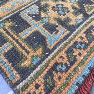 Puede incluir: Primer plano de una alfombra tejida con un patr&oacute;n geom&eacute;trico en tonos de azul, verde, marr&oacute;n y naranja. La alfombra tiene un borde de flecos.