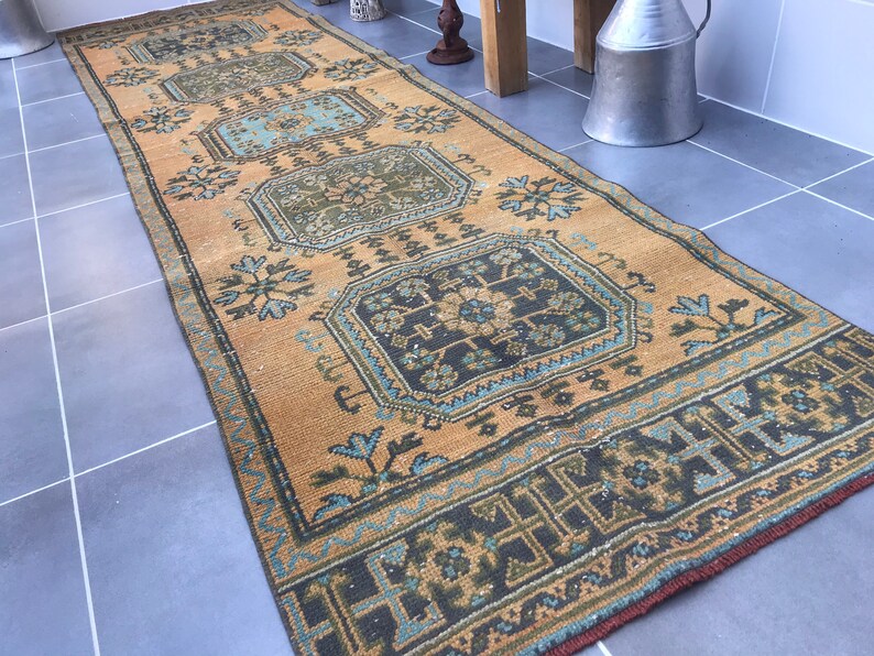 Puede incluir: Una alfombra de pasillo vintage con un fondo beige y patrones intrincados en tonos azules, verdes y negros. La alfombra tiene un aspecto desgastado y es perfecta para agregar un toque de estilo bohemio a cualquier habitaci&oacute;n.