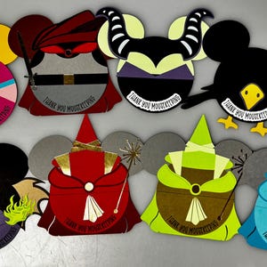 May include: A collection of colorful, die-cut paper crafts in the shape of Mickey Mouse ears, each designed to resemble Disney characters. The designs include villains and princesses, with the text "THANK YOU MOUSEKEEPING" on each.