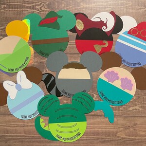 May include: A set of ten Disney character-themed thank you cards. Each card features a different character, including Mickey Mouse, Minnie Mouse, Peter Pan, Captain Hook, Ariel, and more. The cards are decorated with colorful paper cutouts and have the text "Thank You Mousekeeping" printed on them.