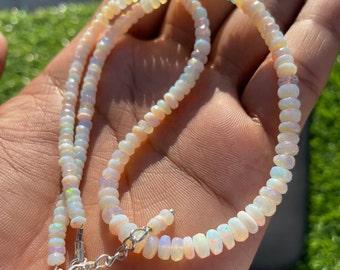 Könnte beinhalten: Halskette aus kleinen Opalperlen mit Silberverschluss. Die Perlen schimmern in Weiß, Creme und blassen Orangetönen. Ein zarter Halsschmuck, der jedem Outfit eine subtile Eleganz verleiht.