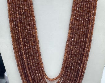 May include: A multi-strand necklace composed of numerous small, faceted, amber-colored beads. The beads are strung together, creating a cascading effect. The necklace is displayed on a white mannequin bust, showcasing its length and design. The beads have a sparkling appearance.