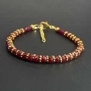Puede incluir: Una pulsera que presenta una alternancia de cuentas de piedras preciosas de color rojo intenso facetadas y pequeños espaciadores de metal dorado. La pieza incluye un cierre de mosquetón dorado y una cadena extensora corta.