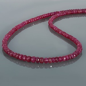 May include: A strand of ruby red gemstone beads strung on a cord. The beads are faceted and have a slightly irregular shape.