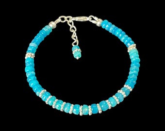 May include: A bracelet featuring round, bright turquoise blue beads alternating with small, metallic silver-toned spacer beads. The piece includes a silver-toned metal chain extension with a lobster clasp and a single matching turquoise bead at the end.